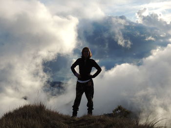 Low angle view of woman standing on hill against cloudy sky