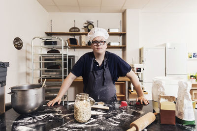 Portrait of confident young baker standing by kitchen counter