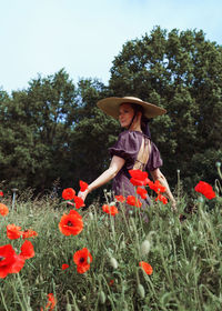 Rear view of woman picking flowers on field against sky