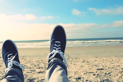 Low section of man sitting on beach against sky