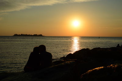 Silhouette people sitting on beach during sunset