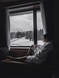 Side view of woman sitting on window