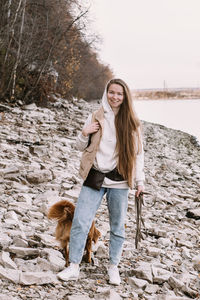 Young woman long hair walking with toller dog at river shore autumn season