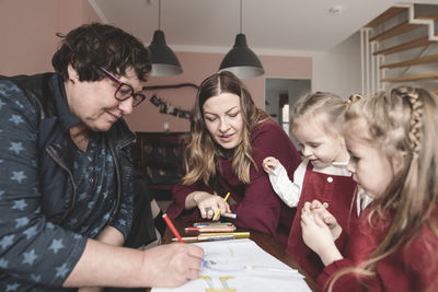 Grandmother, mother and two girls drawing a picture room at home