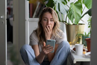 Shocked woman using mobile phone at home