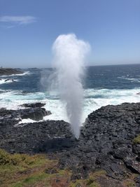 Waves breaking on rocks in sea against sky