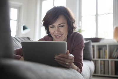 Woman at home lying on the sofa using tablet