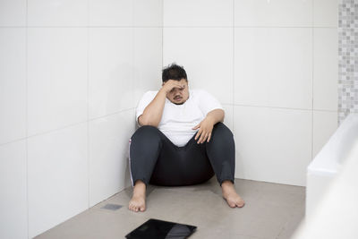 Overweight man sitting with weight scale in bathroom