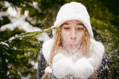 Young woman wearing warm clothing while playing with snow by trees during winter
