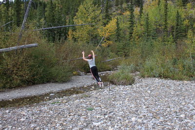 Rear view full length of woman jumping over stream at forest