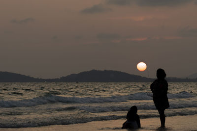 Silhouette people on beach against sky during sunset