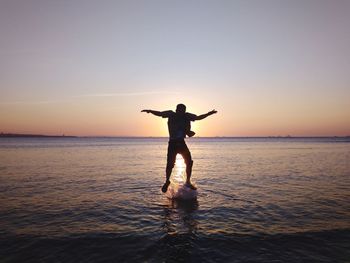 Full length of man jumping in sea against sky during sunset