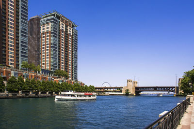 Bridge over river by buildings against clear blue sky