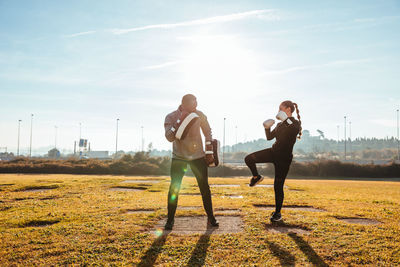 Full length of woman and man exercising on field against sky