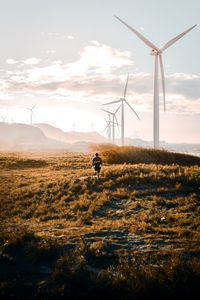 Man walking by wind mill against sky