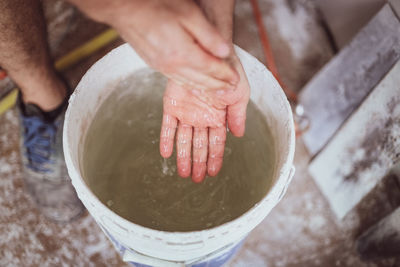 The hands of a young caucasian plasterer are washing in a bucket of water