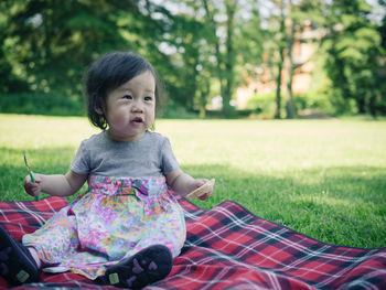 Cute girl eating food while sitting on picnic blanket over grassy field at park