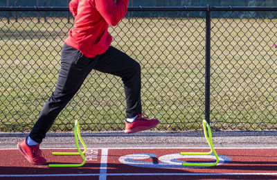 A high school boy is standing over a yellow mini hurdle in the a-position during track practice.