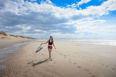 Full length of woman with exercise mat walking on sand at beach against sky