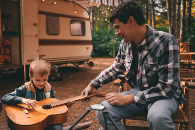 Father teaches son play guitar camping trip  autumn forest camper trailer. fall season outdoors trip