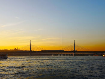 Suspension bridge over sea against sky during sunset