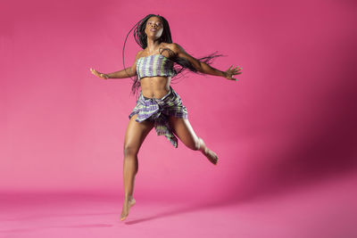 Portrait of young woman dancing against pink background