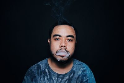 Portrait of young man smoking against black background