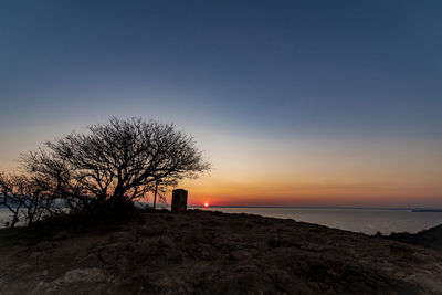 Silhouette bare tree by sea against sky during sunset