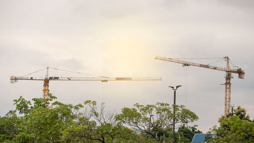 Low angle view of cranes at construction site against sky