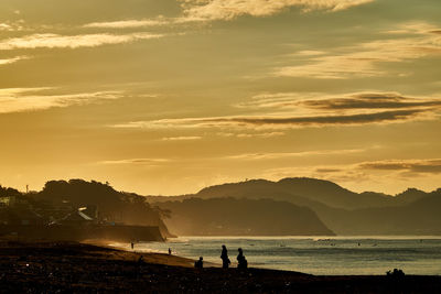 Silhouette people on beach against sky during sunset