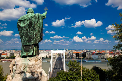 Old statue in front of cityscape against sky
