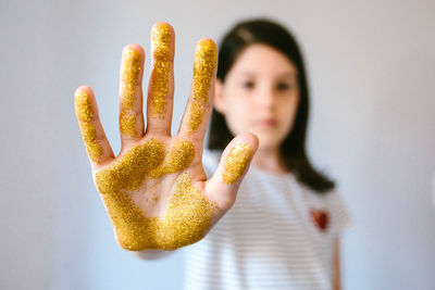 Serious young girl showing her palm hand covered of golden glitter while doing stop sign