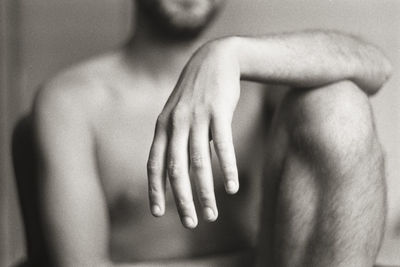 Midsection of naked man sitting against wall at home