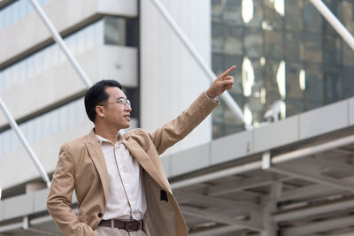 Well-dressed businessman pointing while standing against modern buildings in city