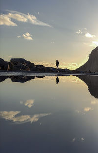 Silhouette person on lake against sky during sunset