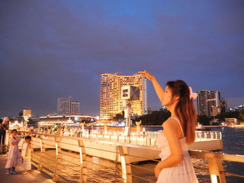 Rear view of young woman sitting on bridge against sky