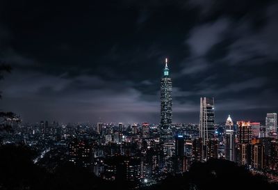 Illuminated buildings against cloudy sky at night