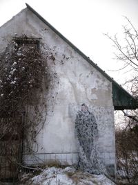 Person standing by abandoned building against sky during winter