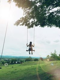 Rear view of girl swinging on field against sky