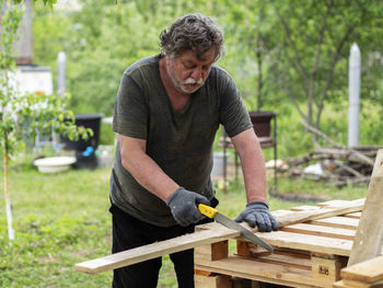 Mature caucasian man sawing a pine board in the garden