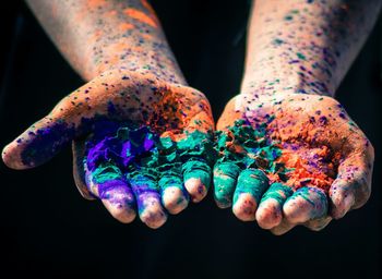 Cropped image of hands with multi colored powder paints over black background