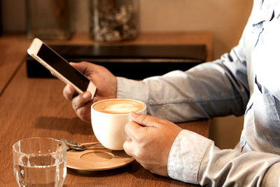 Midsection of man holding coffee cup on table