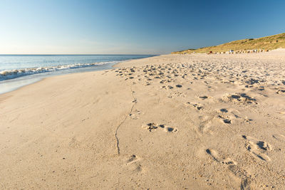 Footprints on sand at beach against clear sky