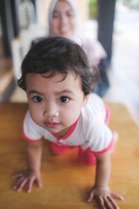 Portrait of cute baby girl kneeling on table