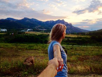 Cropped hand of boyfriend holding girlfriend against mountains during sunset