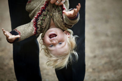 Cropped image of father holding son upside down while standing on field