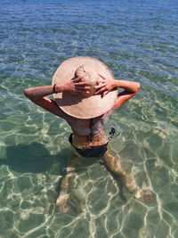 Mature woman in a shallow sea her head covered with hat