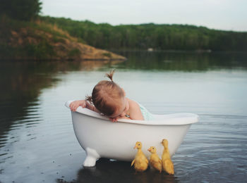 Little baby girl in a bathtub in the lake with three ducklings