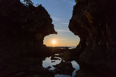 Silhouette rock formations by sea against sky during sunset