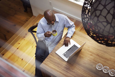 Overhead view of senior man looking at laptop while having coffee in house